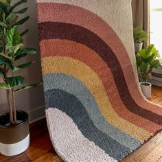 a rainbow rug is on the floor next to a potted plant in front of a window