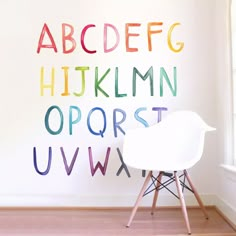 a white chair sitting in front of a wall with letters painted on it and a window