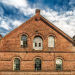 an old brick building with arched windows on the front and second story, against a cloudy blue sky