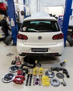 the back end of a white car in a garage with various parts on the floor