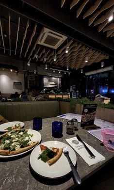 two plates with pizza and silverware on a table in a restaurant at night time