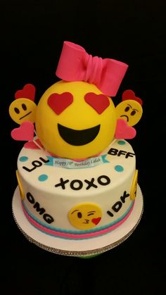 a birthday cake decorated with smiley face emoticions and pink bow on top, sitting on a black surface