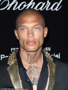 a man with tattoos on his neck and chest standing in front of a black background