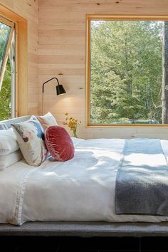 a bedroom with wood walls and windows overlooking the woods