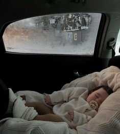 a baby is sleeping in the back seat of a car on a snowy day with his blanket draped over him