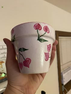 a hand holding a cup with pink flowers painted on it