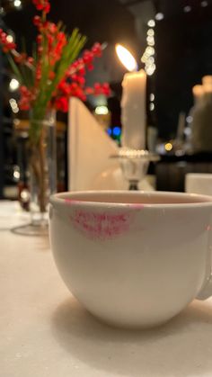 a close up of a cup on a table with a lit candle in the background