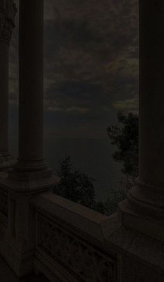 an empty balcony with columns and pillars under a cloudy sky at night, overlooking the ocean