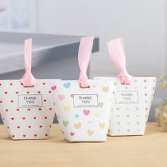 three small bags with pink bows on them sitting on a table next to some flowers