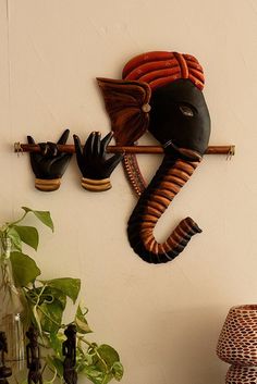 an elephant head mounted to the wall with two hands on it's back and one hand holding a stick