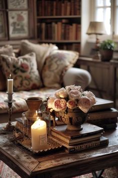 a coffee table with books, candles and flowers on it in front of a couch