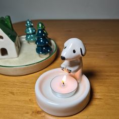 a white dog figurine sitting on top of a table next to a lit candle