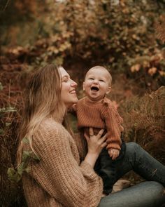 a woman holding a baby in her arms and laughing at each other while sitting on the ground