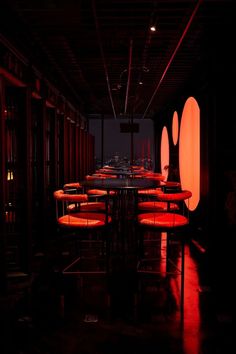 a dimly lit room with round tables and orange chairs in the center, surrounded by red lights