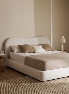 a white bed sitting on top of a wooden floor next to a lamp and window