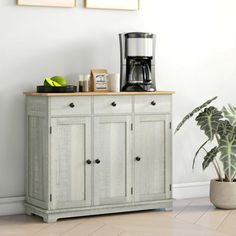 a white cabinet with two green plants on top and a black coffee maker above it