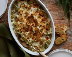 a casserole dish with cheese and artichokes on the side next to bread