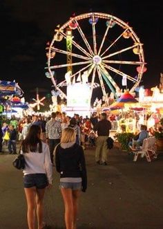 two girls standing in front of a carnival at night with ferris wheel in the background