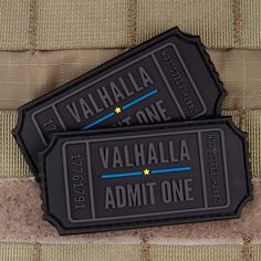 two black luggage tags sitting on top of a piece of fabric with the words valhalla admit one