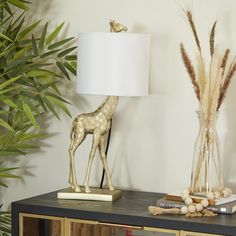 a giraffe lamp sitting on top of a table next to a vase filled with plants