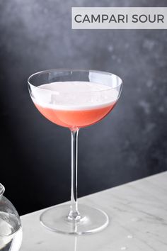 a pink drink in a coupe glass on a marble countertop with the words campari sour above it