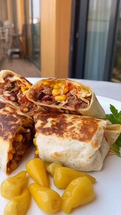 two burritos cut in half on a white plate with yellow peppers next to them