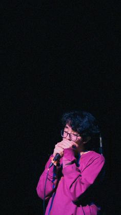 a man standing in front of a microphone with his hands on his face and wearing glasses