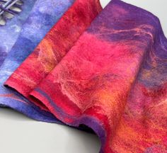 Experience the beautiful drape and softness  of this super lightweight handmade Nuno felt scarf/wrap in variegated colors of red/purple.  Made using a process called wet felting.   Created with a lightweight silk on one side, merino wool and silk hanky on the surface.  The hand is soft to the touch and you will love wearing this wrap to dress up or with a pair of jeans.   Light and airy with year round wear capability.    Specs: 60"l x 10.5"w Care:  Hand wash in cold water using mild detergent specifically for wool, rinse well, gently squeeze excess water out then roll in towel to remove any remaining, lay flat to dry.  Do not wring out.  Gently shape back to its original shape.  Can touch up with a light iron if needed, but please make sure temperature is on low heat.  Dry flat. Please no Mindful Crafts, Evening Wrap, Felt Fashion, Felt Scarf, Evening Wraps, Nuno Felt Scarf, Felted Scarf, Nuno Felt, Wet Felting Projects