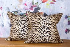 two leopard print pillows sitting on top of a wooden table next to a flowered wall