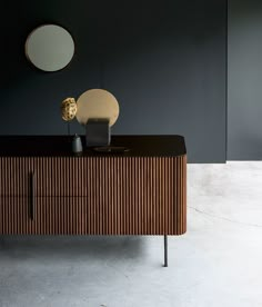 a wooden cabinet with two round mirrors on it's sides and a black wall in the background