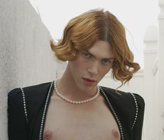 a woman with red hair wearing pearls and a black top is standing in front of a wall