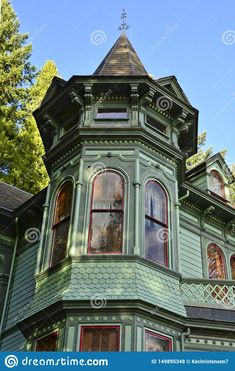 an old victorian style house with green paint and red trim on the windows, surrounded by trees