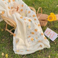 a blanket and book laying on the grass next to a wicker basket with sunflowers