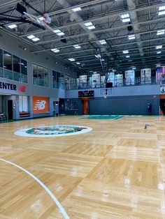 an indoor basketball court with hard wood flooring and lights on the ceiling, surrounded by large windows