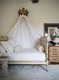 a canopy bed with white sheets and pillows in a small room next to a dresser