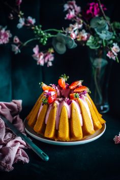 a bundt cake with strawberries and icing on a plate next to flowers