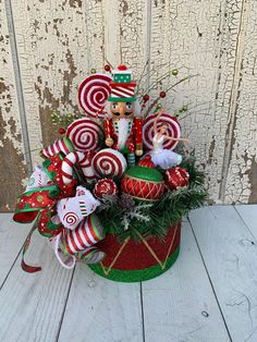 a christmas arrangement with candy canes and ornaments in a green basket on a white wooden surface