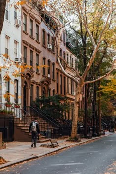 a man is walking down the street in front of some brownstone buildings and trees