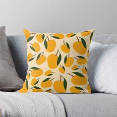 a yellow pillow with oranges on it sitting on a gray couch next to pillows