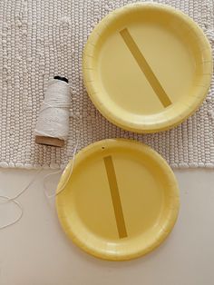 two yellow paper plates sitting on top of a table next to a spool of thread