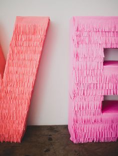 two pink letters with fringes on them are next to each other in front of a white wall