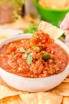 a hand dipping a tortilla chip into a bowl of salsa surrounded by tortilla chips