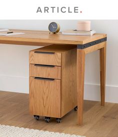 a wooden desk with two drawers and a clock on the top, in front of a white wall