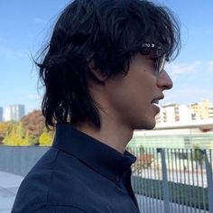 a man with black hair and glasses standing in front of a fence looking off into the distance