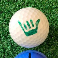 two golf balls with green hand prints on them and one blue is in the grass