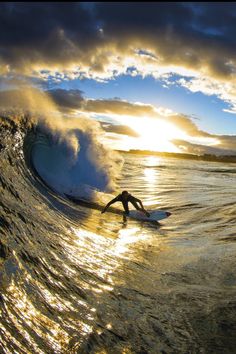 a man riding a wave on top of a surfboard in the ocean at sunset