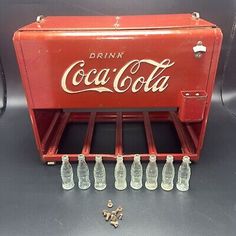 an old coca - cola machine with six empty bottles and screws on the table