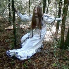 a woman dressed in white is sitting in the woods with her arms spread wide open