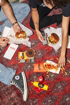 two people sitting on the floor eating hot dogs and hamburgers with ketchup