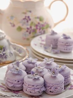 there are many purple desserts on the plates next to tea cups and saucers